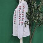 Detaliu broderie florală pe mâneca unei ii tradiționale de femei, cu motive roșii și negre pe bumbac alb.