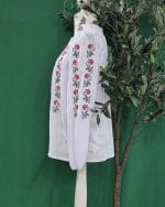 Detaliu broderie florală pe mâneca unei ii tradiționale de femei, cu motive roșii și negre pe bumbac alb.